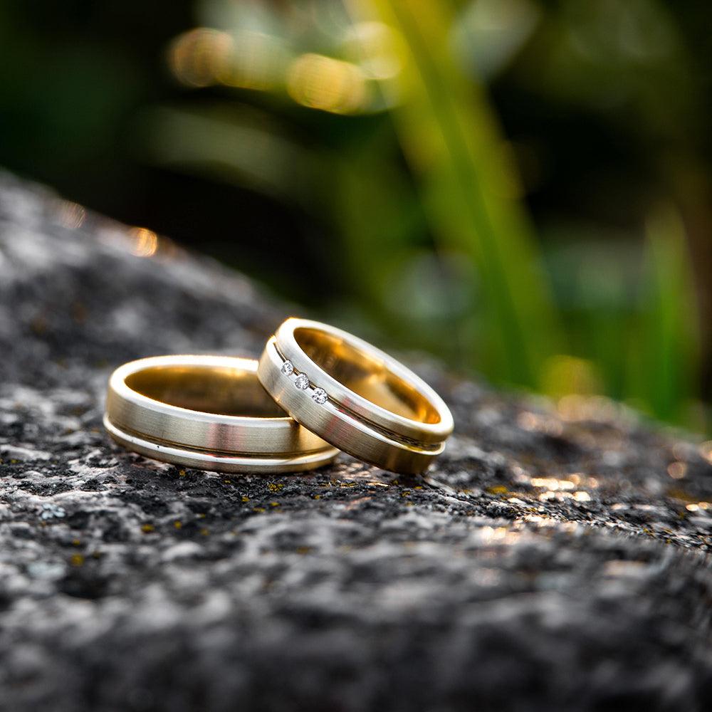 A pair of wedding rings set on top of each other on a stone with blurry plants in the background