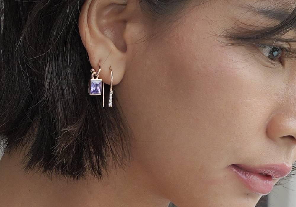  A woman laying on a backdrop of plants staring up into the camera, on her left hear she is wearing a ruby earring